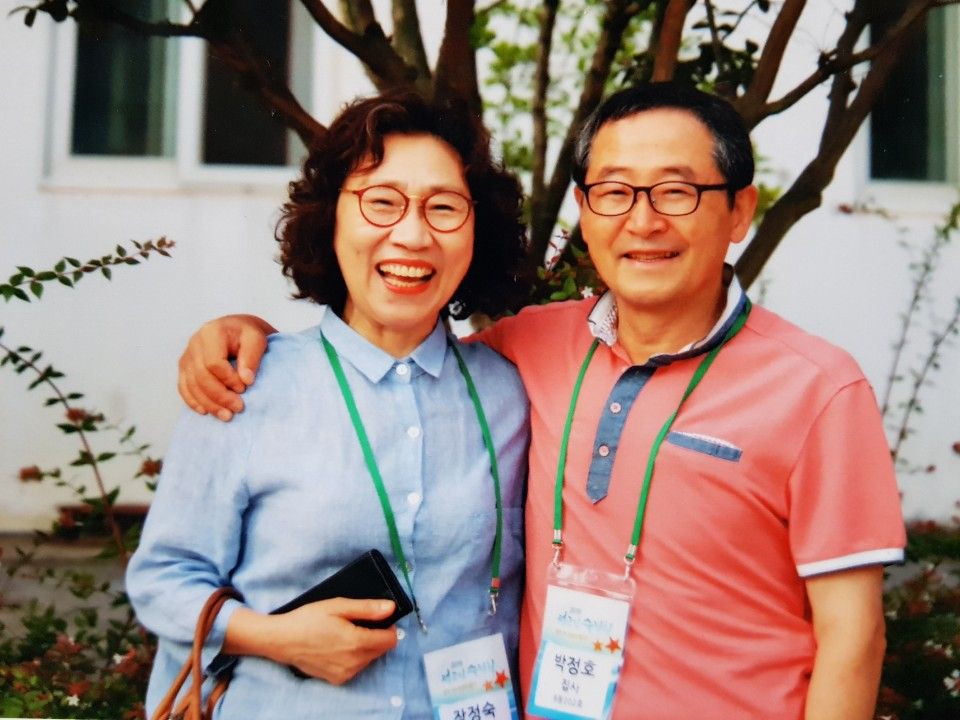 이름표를 목에 걸고 어깨동무한 채 활짝 웃는 두 사람